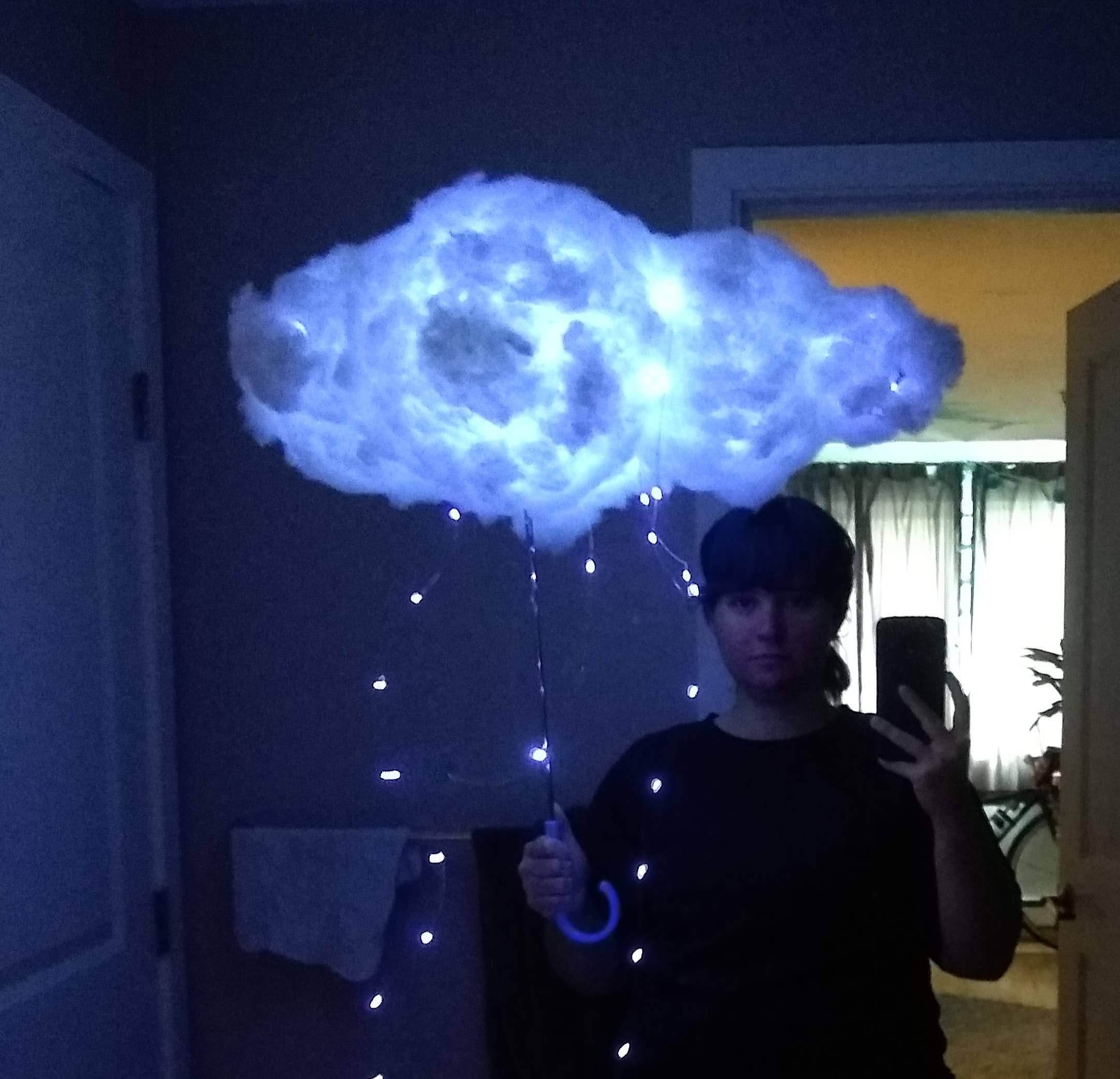 someone holding a lightning storm cloud umbrella art piece with a few string lights hanging down past the umbrella handle