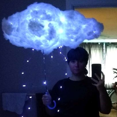 someone holding a lightning storm cloud umbrella art piece with a few string lights hanging down past the umbrella handle