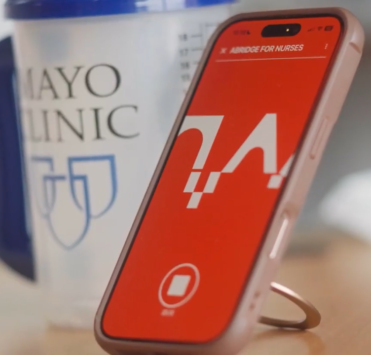 a mayo clinic tumbler and a phone with the abridge active recording screen on a small table or desk